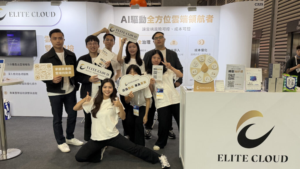 Group of people at an Elite Cloud exhibition booth posing with signs and thumbs up, wearing white shirts and lanyards.